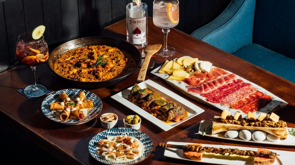 Spaanse tapasavond met warme potjes, paella, vlees, kaas en charcuterie op houten tafel.
