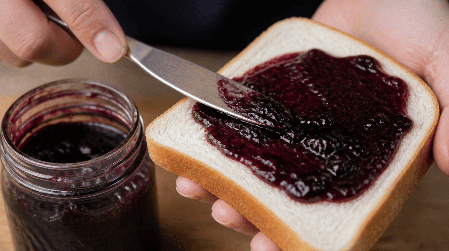 Iemand smeert bramenjam op een boterham
